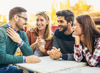 Four people sitting around a table outside talking