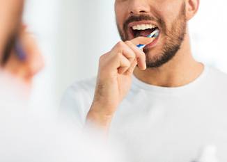 Nose-to-chest shot of man in white shirt brushing teeth in front of mirror