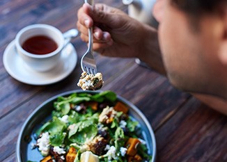 Man eating a salad with tea at a wooden table
