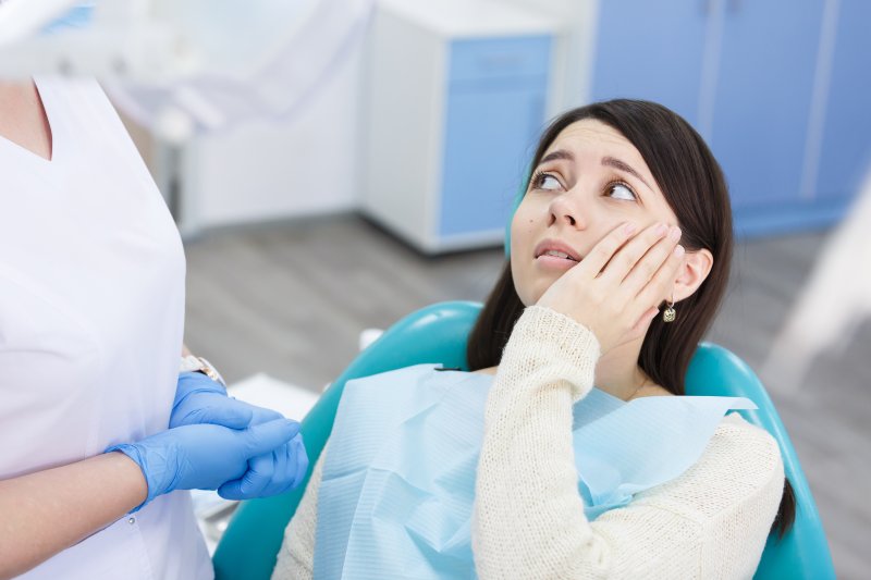 A concerned woman holding her cheek while seeing her dentist